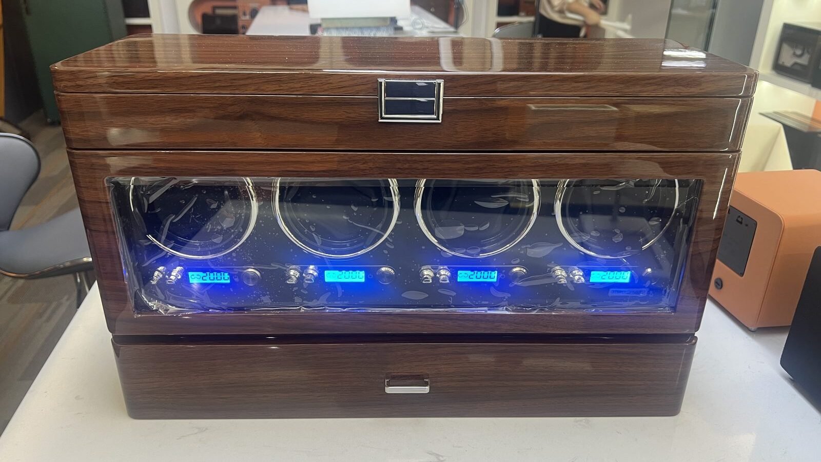 Four-slot walnut watch winder with glass door and blue LCD displays, front view