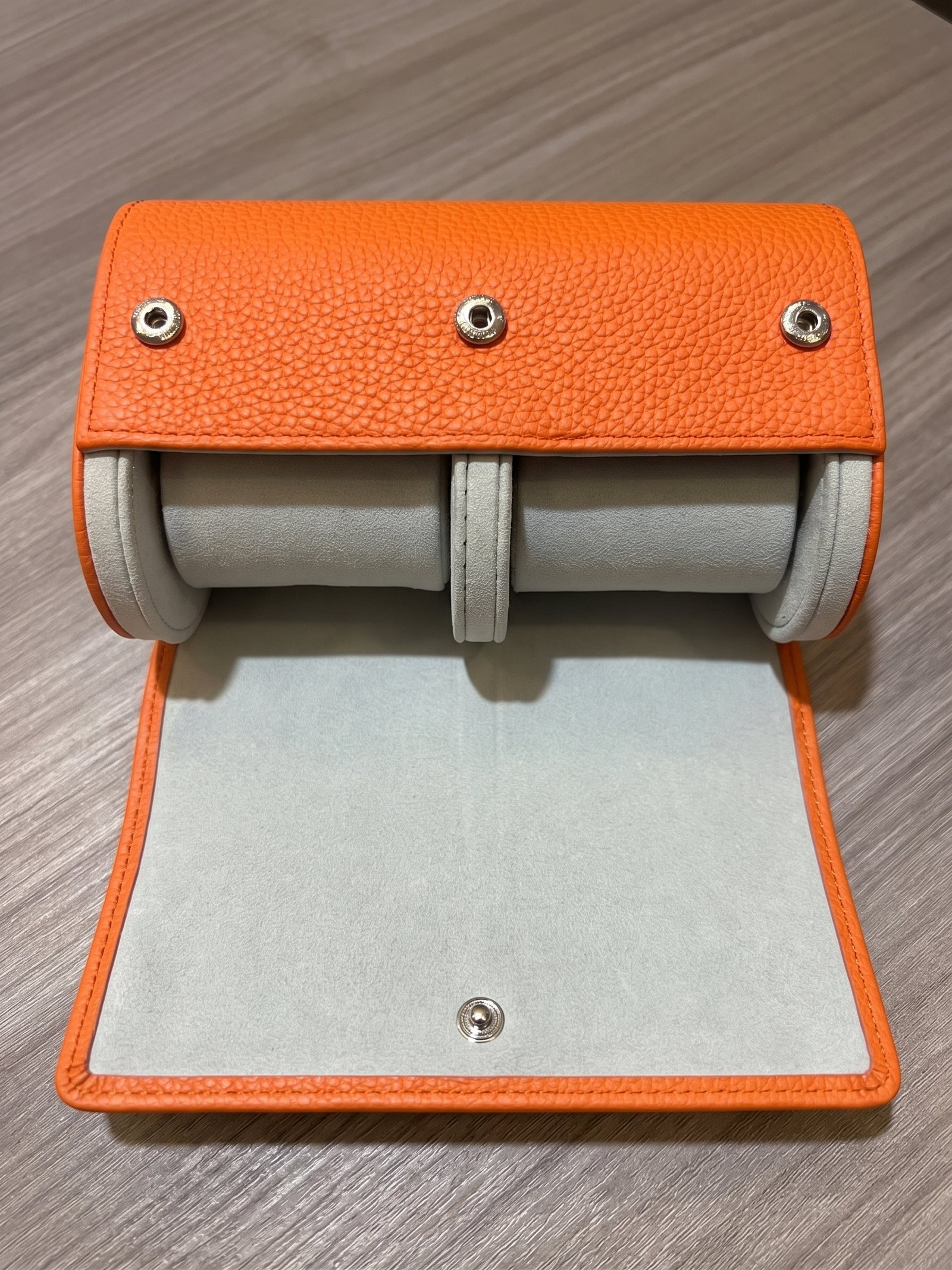 Open orange two-watch roll showing two light-colored cushions, a central divider, and snap fasteners.