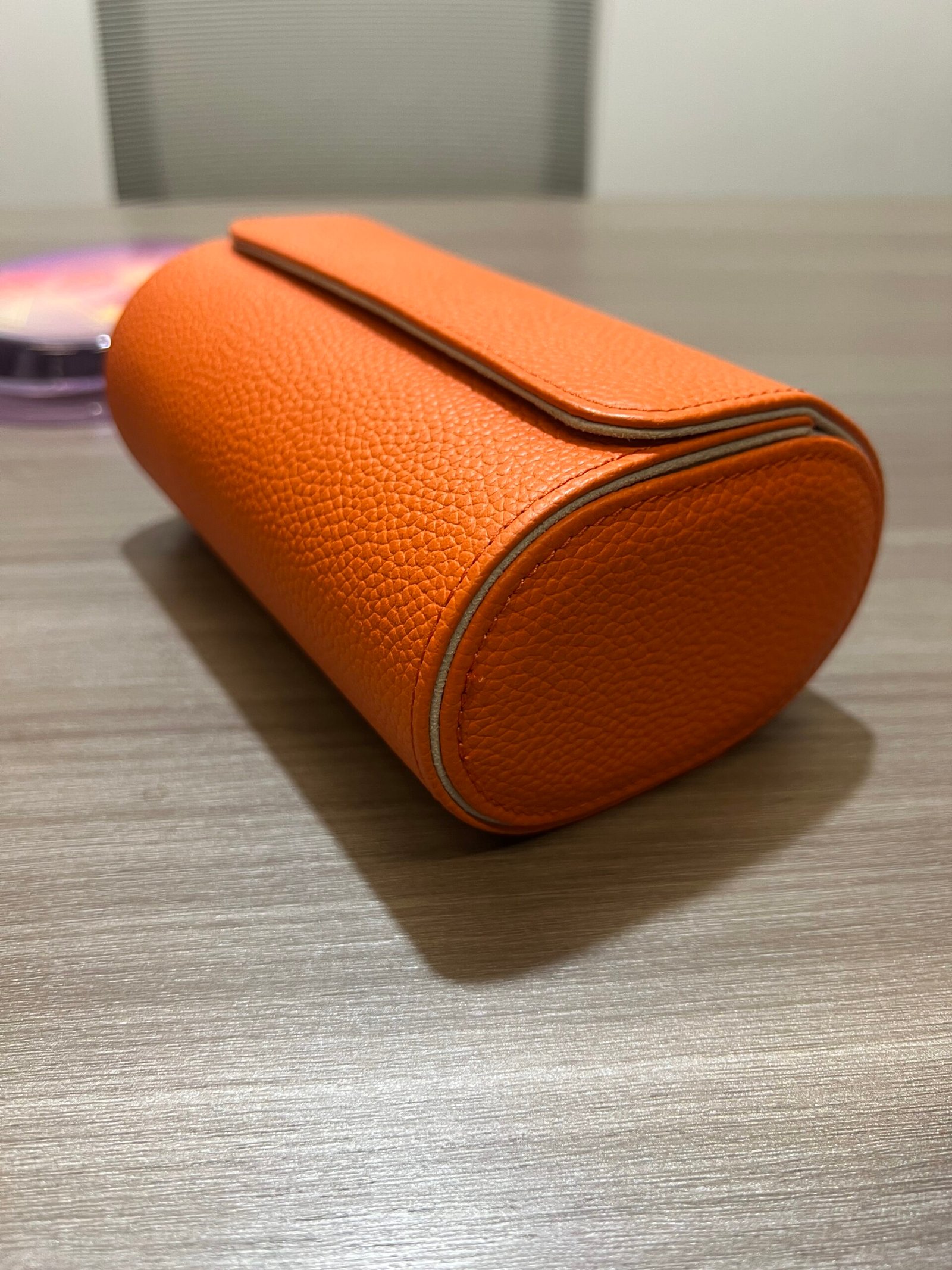 Closed orange textured watch roll lying on a tabletop, viewed from the side.