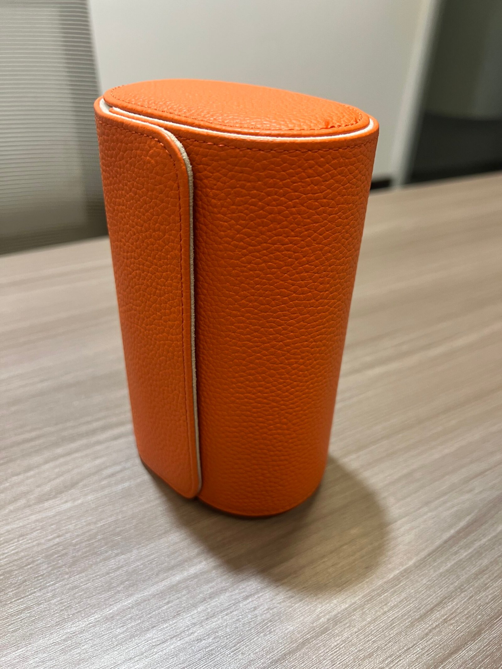 Closed orange textured watch roll standing upright on a tabletop.